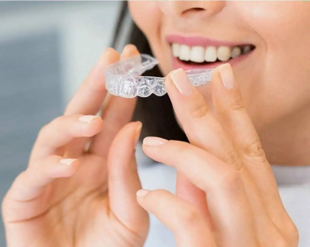 Picture of a woman at a dentist near Raleigh putting in clear aligners wondering how does Invisalign work?